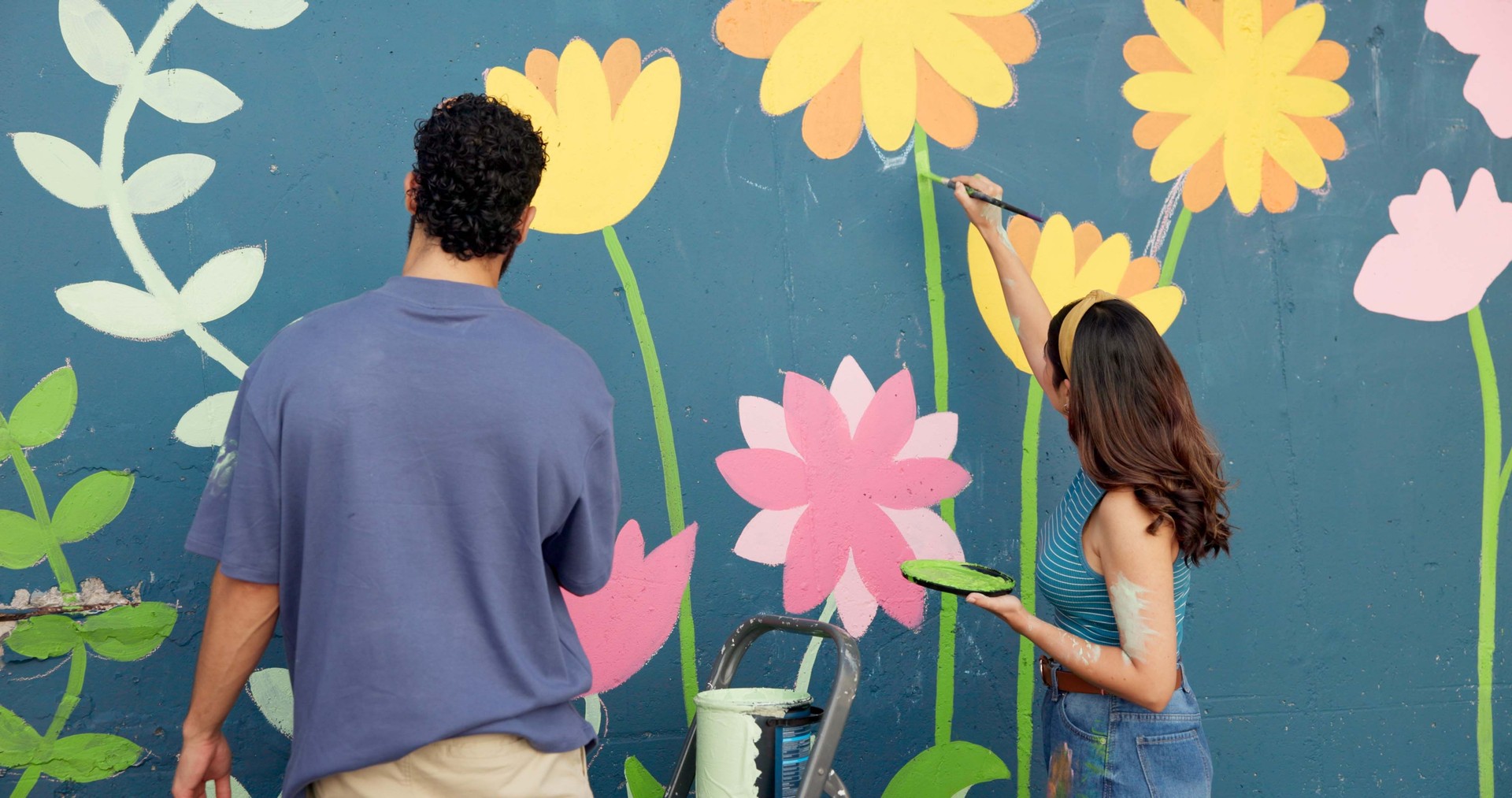 Back, couple and painting on wall for art project, mural design and renovation of community. People, artist and hobby for creativity improvement, diy decoration and expression with flowers aesthetic